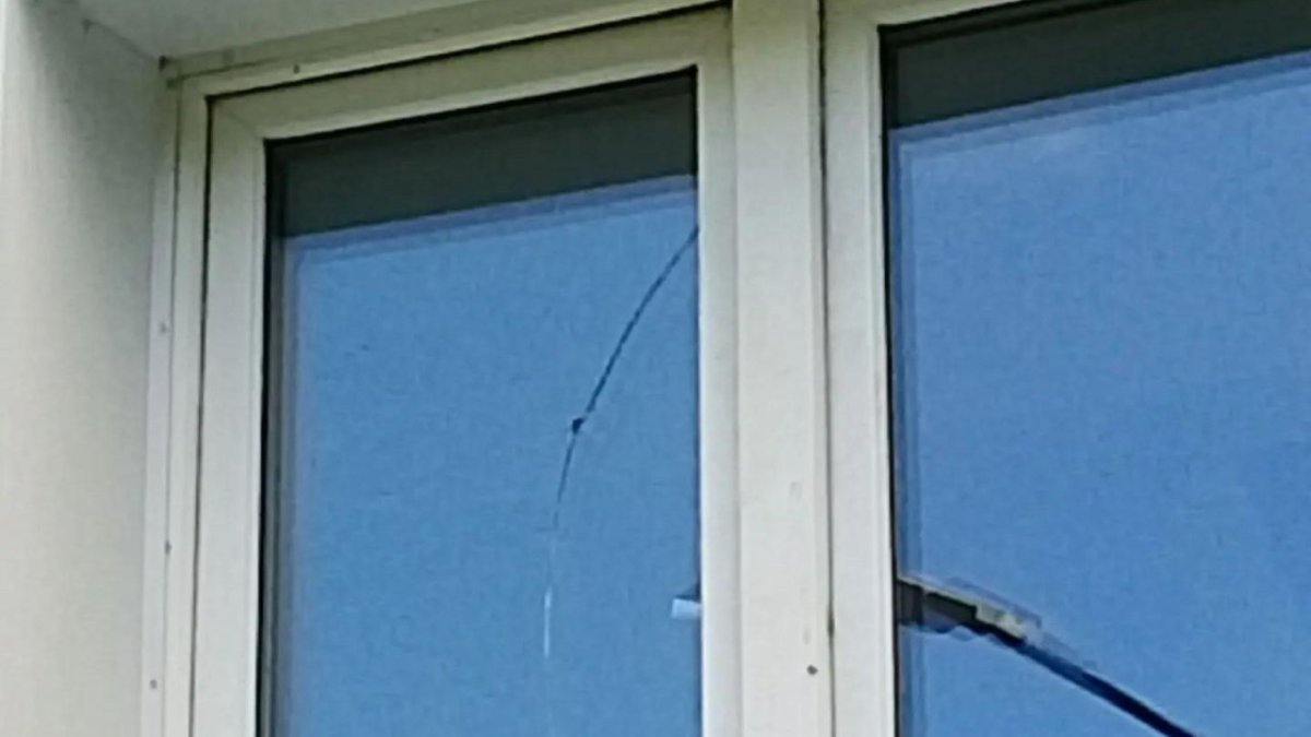 Дыра от пули в окне стеклопакета жилого дома