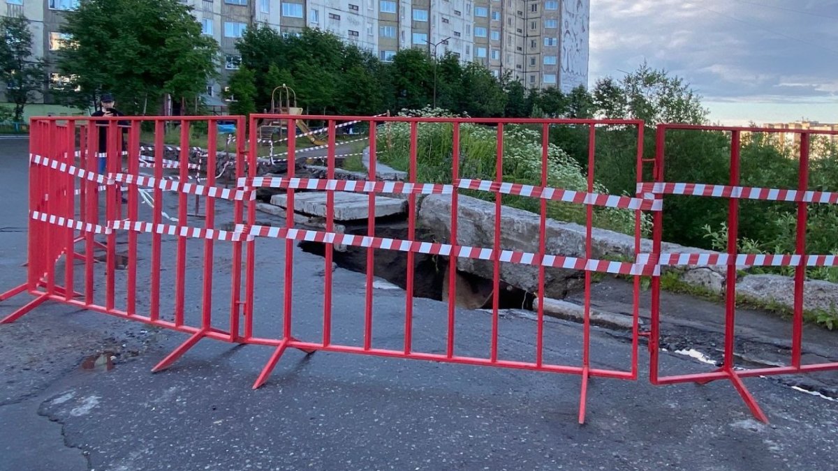 Дыра в асфальте летом ограждена лентой и забором