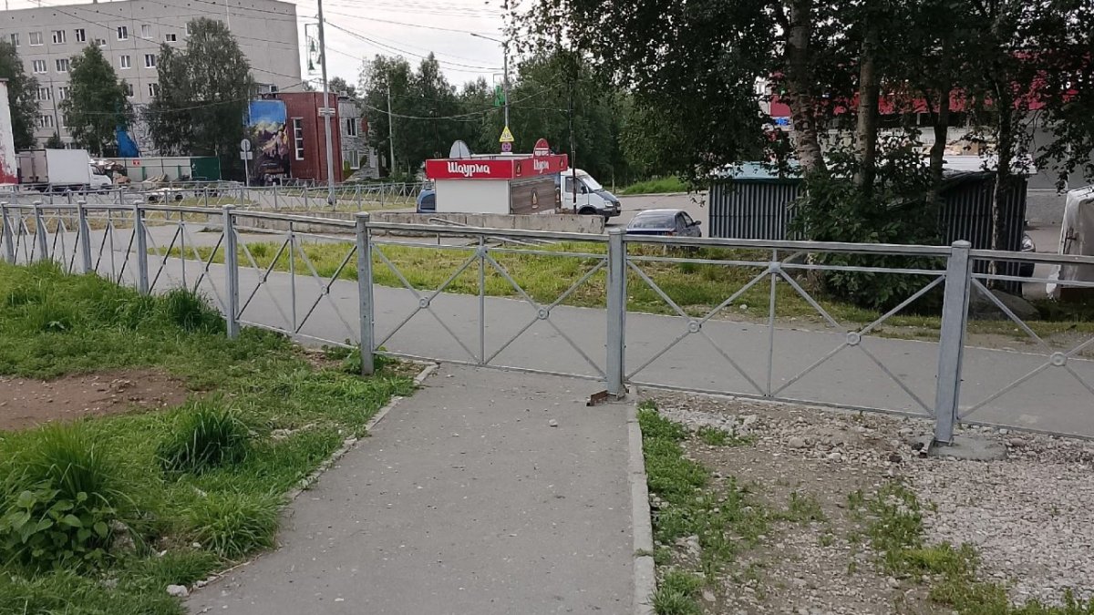 Забор и тротуар на фоне жилых домов летом