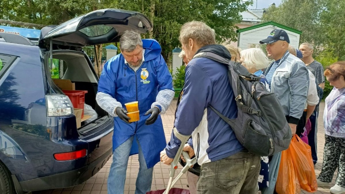 Мужчина передает другому мужчине суп в пластиком контейнере на улице летом.