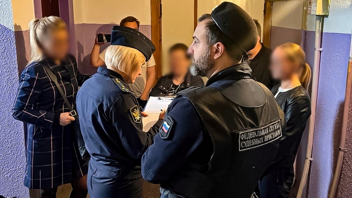 Судебные приставы и жители дома стоят в подъезде.